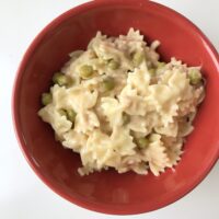 Bowtie Macaroni and cheese pasta with tuna fish and peas in a red bowl.