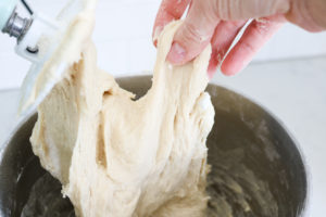 dinner roll dough in electric stand mixer with a hand holding dough