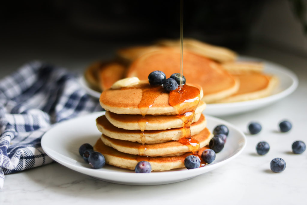 Gluten Free Pancakes from Bob's Redmill pancake mix with blueberries and syrup pouring on top