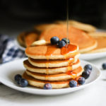 Gluten Free Pancakes from Bob's Redmill pancake mix with blueberries and syrup pouring on top