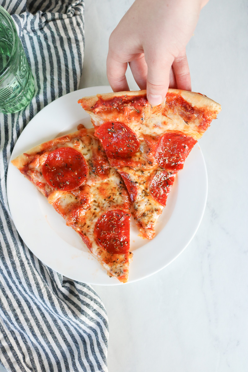 2 slices of homemade pizza with hand holding pizza