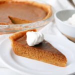 slice of pumpkin pie with whipped cream on top on a white plate