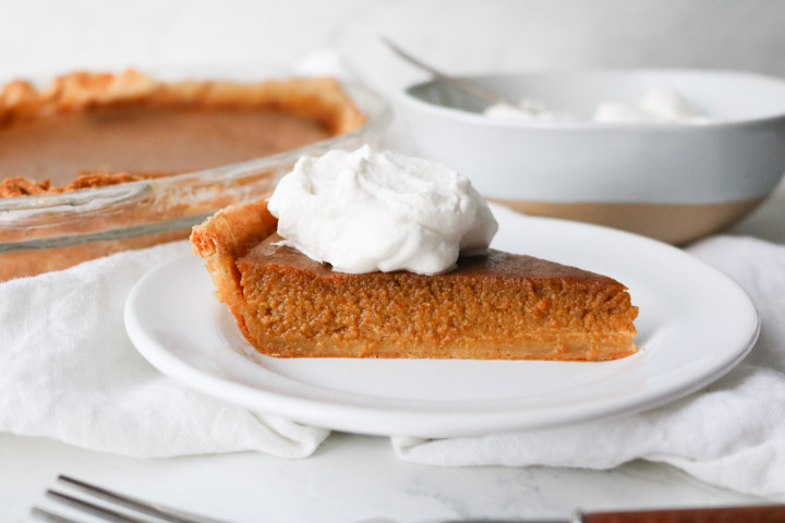 slice of pumpkin pie with whipped cream on top on a white plate